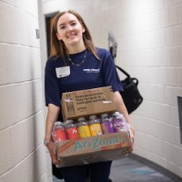 GVSU Alumna smiles as she carries Arizona Tea box through the dorm hallways